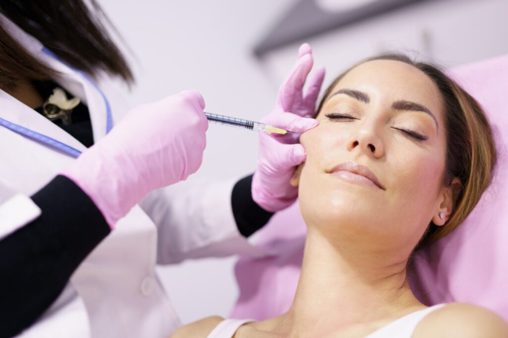 Doctor injecting hyaluronic acid into the cheekbones of a woman as a facial rejuvenation treatment